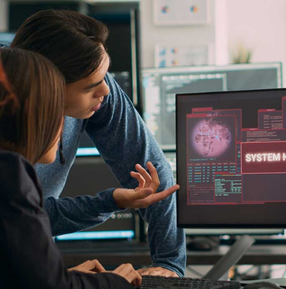 Two software engineers analyzing system data and cybersecurity dashboard on computer monitors in a modern tech workspace