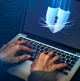 Hands typing on a laptop with a glowing blue digital shield and keyhole icon on the screen, representing cybersecurity and data protection.