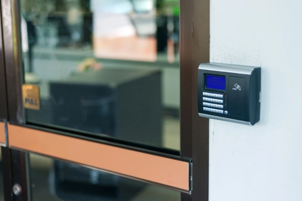 Electronic keypad door access control system mounted on a wall next to an office glass door.